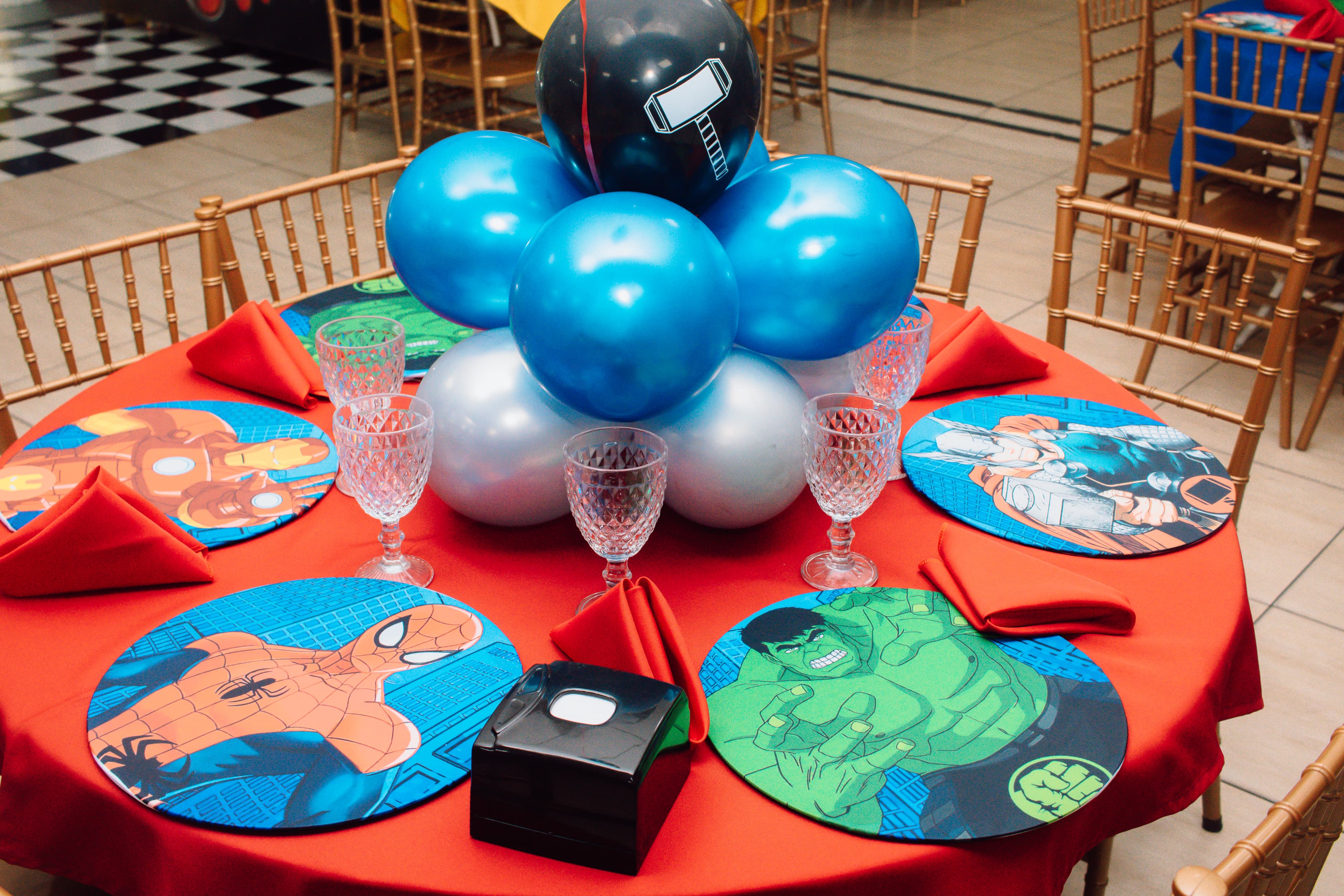Mesa posta completa com sousplats temáticos dos Vingadores, guardanapos e taças de cristal